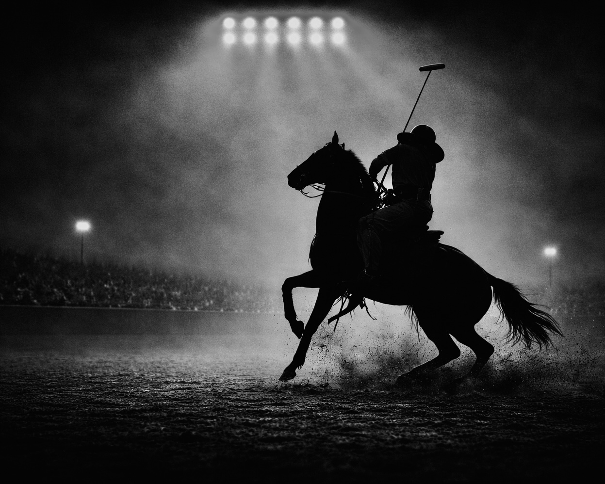 Cowboy polo match in a dirt arena under arena lights